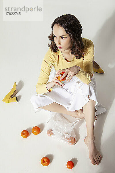Young woman holding tangerines sitting on floor at studio