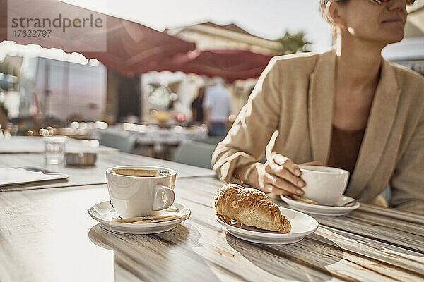 Frau hält Kaffeetasse in der Hand und sitzt an einem sonnigen Tag im Straßencafé