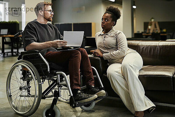 Geschäftsfrau hört im Büro einem behinderten Kollegen im Rollstuhl zu