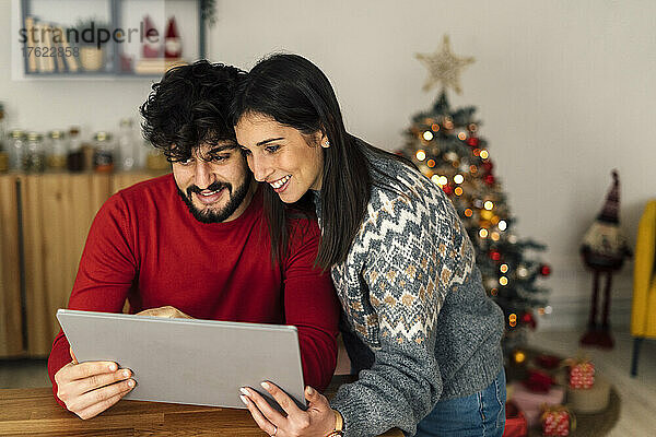 Lächelndes junges Paar blickt im Wohnzimmer auf den Tablet-PC