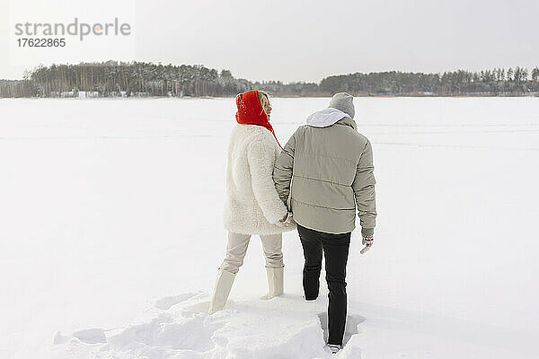 Paar hält sich an den Händen und geht im Winter auf Schnee