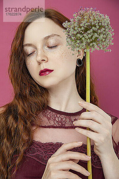 Frau mit geschlossenen Augen hält Blume vor rosa Hintergrund