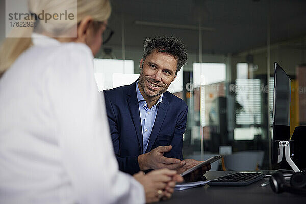 Lächelnder Geschäftsmann diskutiert über Tablet-PC mit Kollegen im Büro