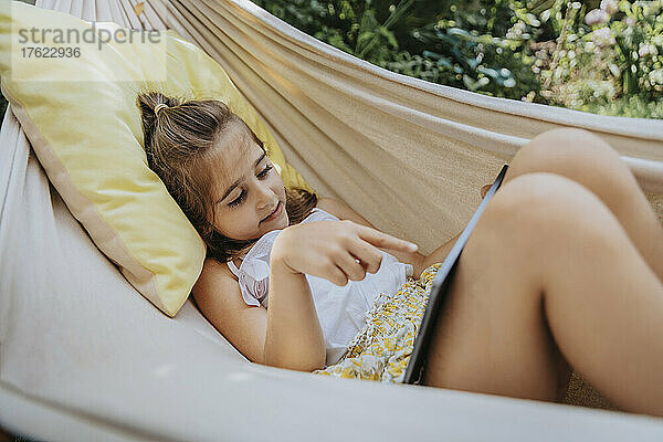 Girl with tablet PC lying in hammock