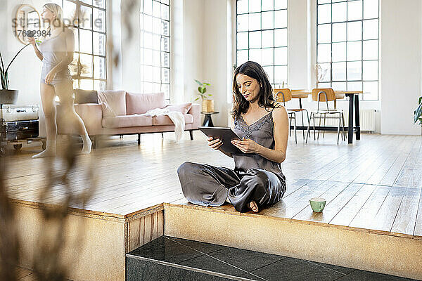 Geschäftsfrau mit Tablet-PC sitzt zu Hause auf der Diele im Wohnzimmer