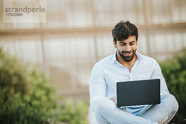 Lächelnder Freiberufler mit Laptop im Freien