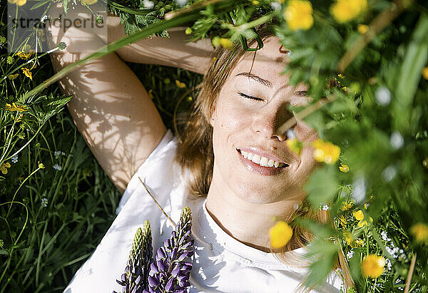 Smiling woman with eyes closed lying on grass on sunny day