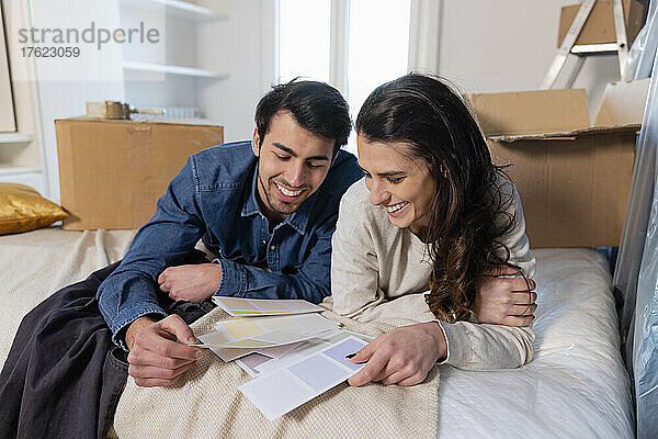 Lächelndes junges Paar wählt Farbmuster im Schlafzimmer seines neuen Zuhauses