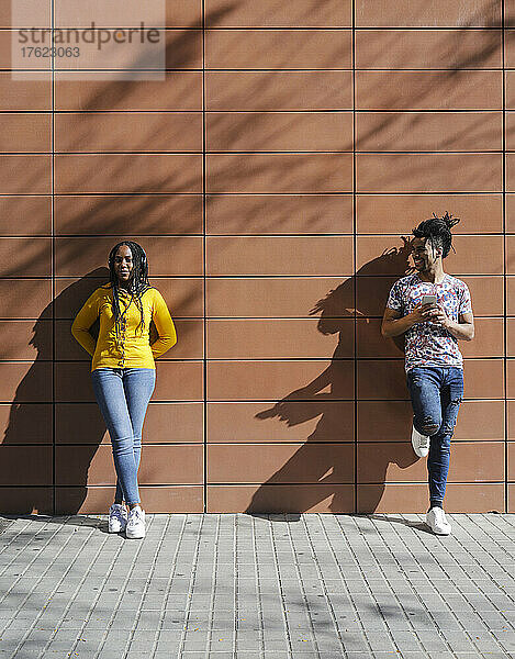 Junger Mann schaut Freundin an  die an einem sonnigen Tag vor der Wand steht