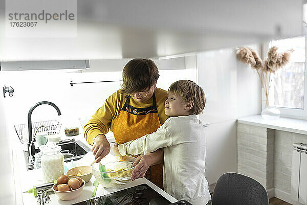 Glücklicher Enkel umarmt Großmutter in der heimischen Küche