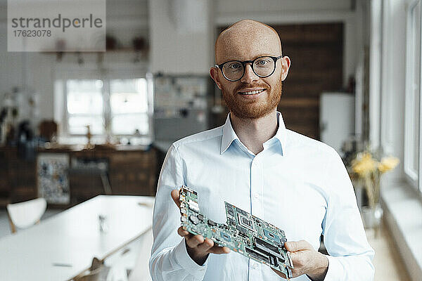 Smiling young businessman standing with circuit board in office