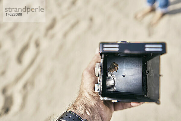 Man holding vintage camera with picture of woman at beach