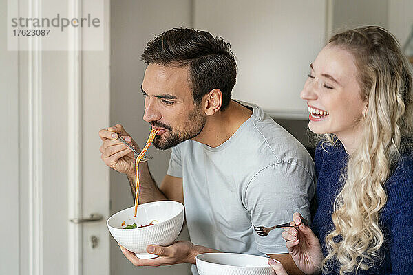 Glücklicher junger Mann  der zu Hause von einer fröhlichen Freundin Spaghetti isst