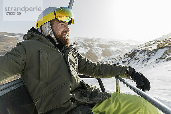 Lächelnder junger Mann mit Bart sitzt am Skilift