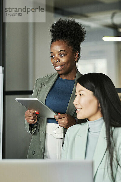 Geschäftsfrau mit Tablet-PC schaut Kollegen im Büro an