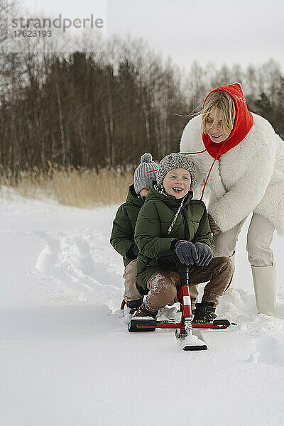 Glückliche Mutter schiebt ihre Söhne im Winter auf der Rodel