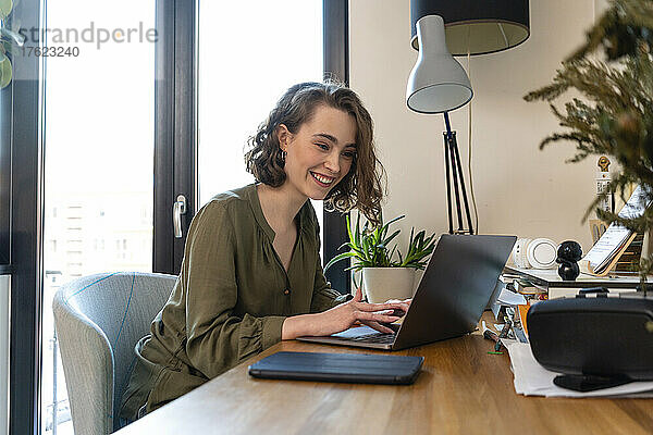 Lächelnde junge Frau mit Laptop am Tisch sitzend
