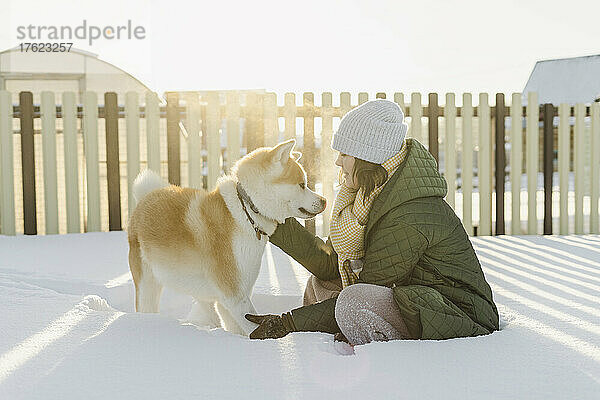 Frau mit Hund im verschneiten Garten im Winter