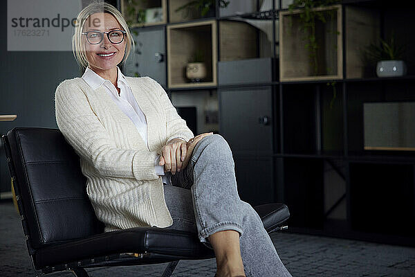 Glückliche Geschäftsfrau mit Brille sitzt am Arbeitsplatz