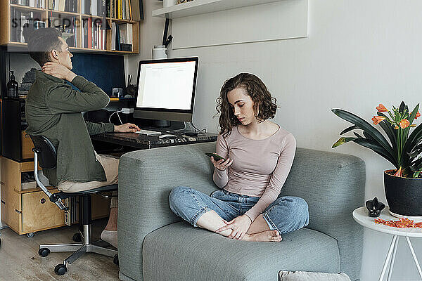 Junger Mann nutzt Desktop-PC  während Frau zu Hause über Smartphone im Internet surft