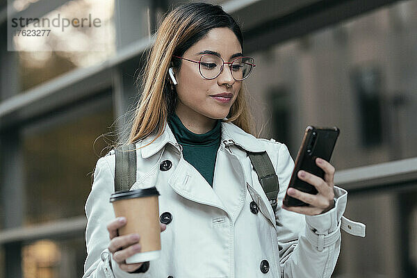 Frau hält Einwegbecher und benutzt Mobiltelefon