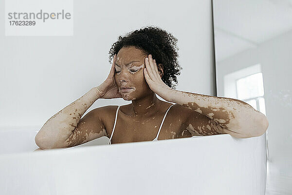 Frau sitzt zu Hause in der Badewanne und hat Kopfschmerzen