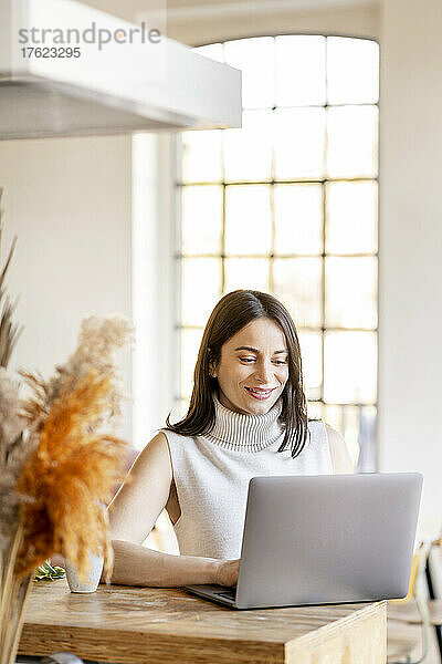 Lächelnde junge Frau  die zu Hause am Laptop arbeitet