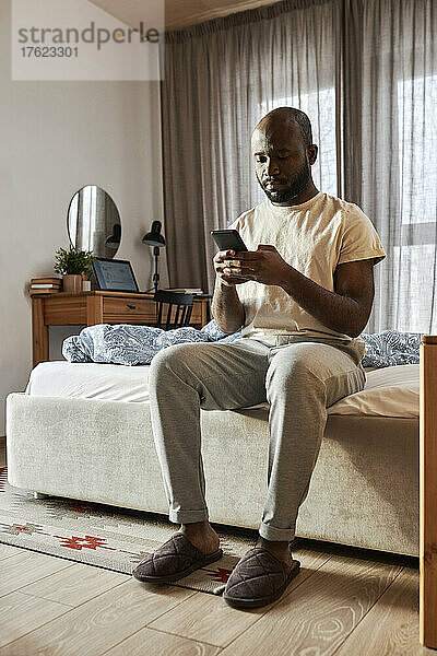 Mann benutzt Smartphone  sitzt morgens zu Hause im Bett