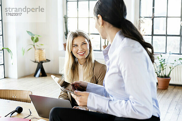 Glückliche blonde Geschäftsfrau blickt auf einen Kollegen  der einen Tablet-PC hält
