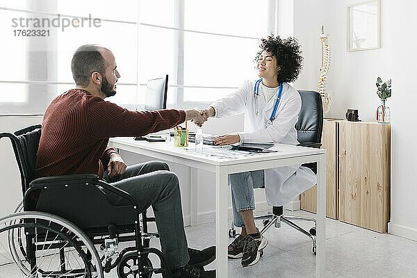 Behinderter Patient sitzt im Rollstuhl und schüttelt dem Arzt in der Klinik die Hand