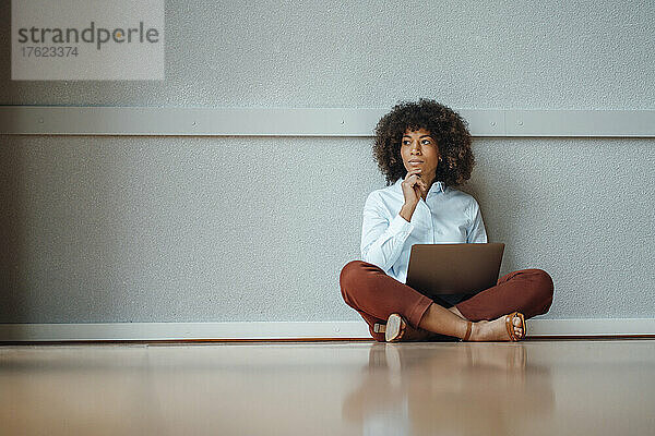 Nachdenkliche Geschäftsfrau mit Laptop sitzt am Arbeitsplatz auf dem Boden