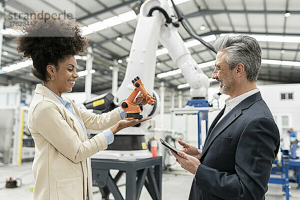 Lächelnder Entwickler zeigt Geschäftsmann in Fabrik Modell eines Roboterarms