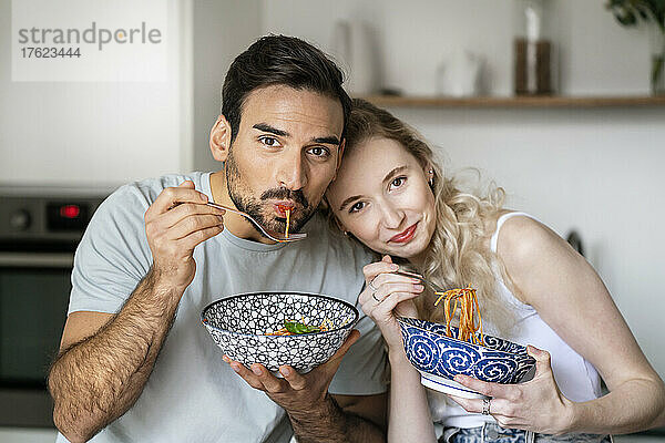 Lächelnder Mann und Frau essen zu Hause Spaghetti
