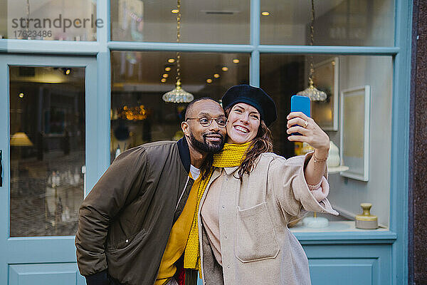 Lächelndes Paar macht Selfie mit Smartphone vor Café