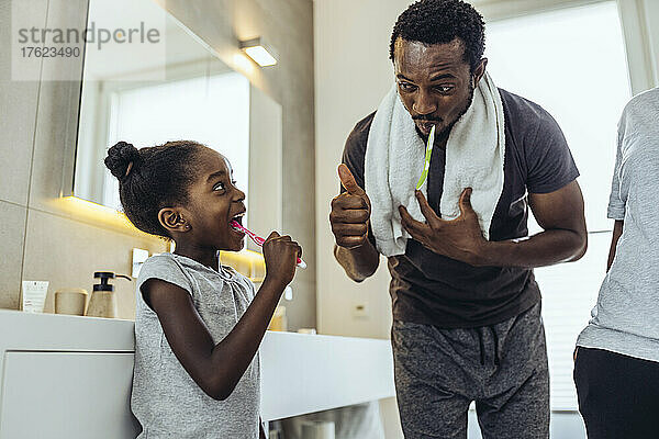 Vater zeigt Tochter beim Zähneputzen im Badezimmer die Daumen