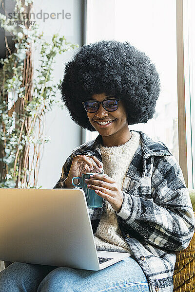 Lächelnde Geschäftsfrau mit Tasse und Laptop auf dem Schoß