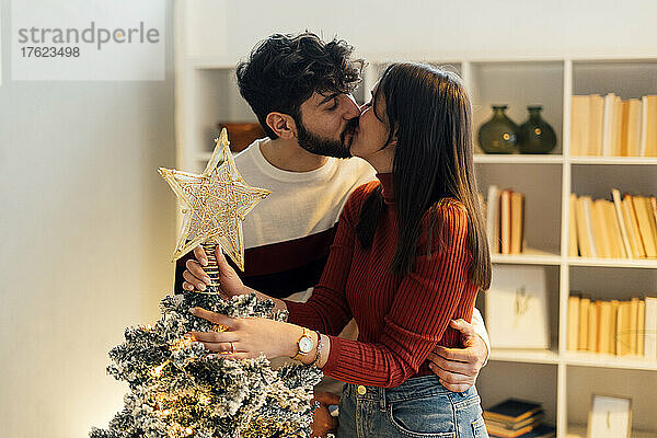 Liebevolles Paar küsst sich zu Hause vor dem Weihnachtsbaum