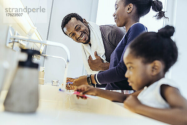 Smiling father washing toothbrush by daughters in bathroom