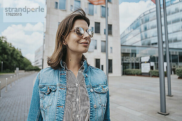 Frau in Jeansjacke mit Sonnenbrille vor Gebäude