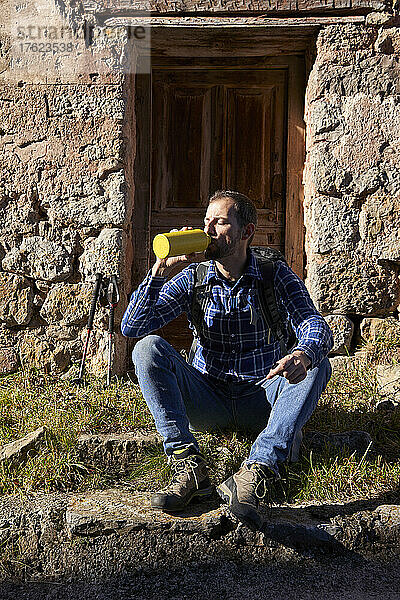 Mann trinkt Wasser aus gelber Flasche und sitzt vor der Tür