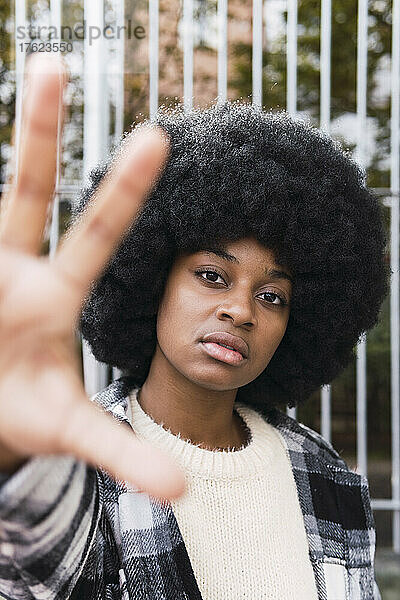 Junge Afro-Frau zeigt Palme vor Zaun
