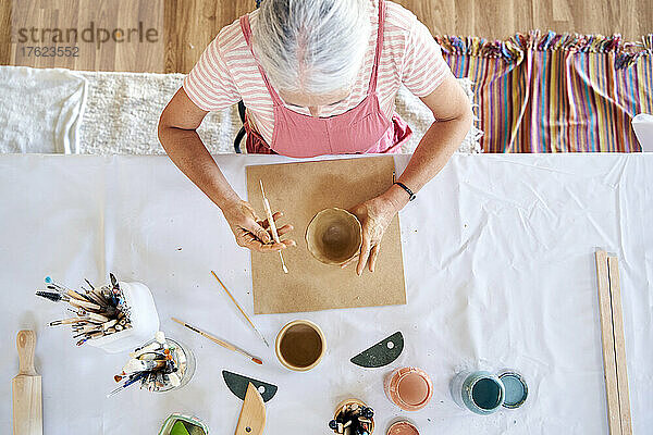 Artist painting homemade clay pot at table