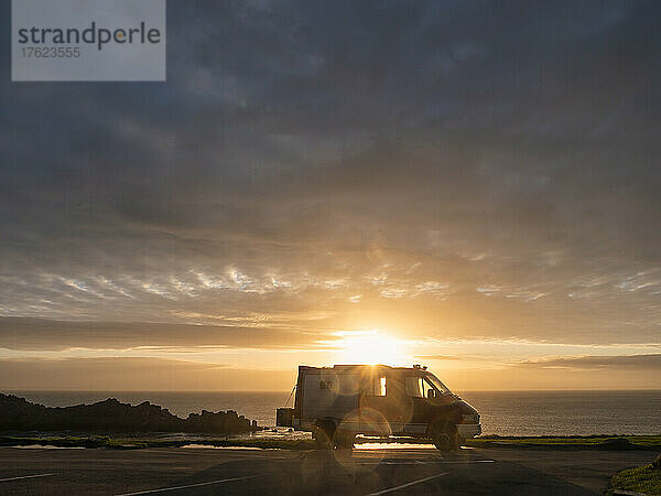 Silhouette eines Lieferwagens  der vor der untergehenden Sonne über der Landzunge Pointe du Grouin steht
