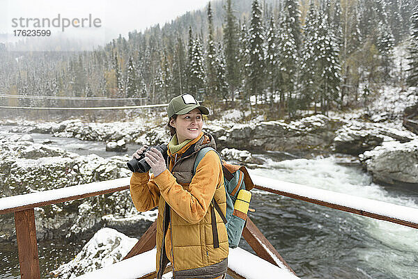 Glückliche Frau mit Fernglas genießt das Wochenende am Fluss im Winter
