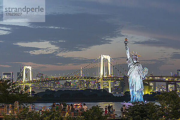 Japan  Kanto-Region  Tokio  Nachbildung der Freiheitsstatue und beleuchtete Regenbogenbrücke in der Abenddämmerung