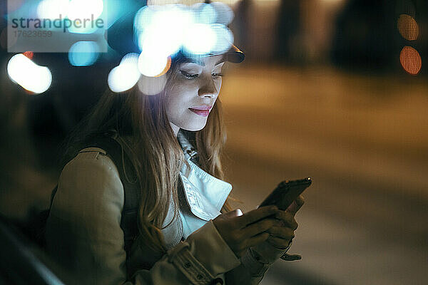 Beautiful woman wearing cap using mobile phone at night