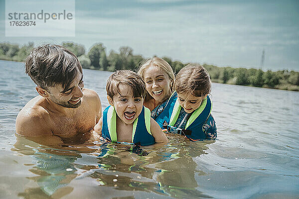 Fröhliche Eltern schwimmen mit Kindern im See