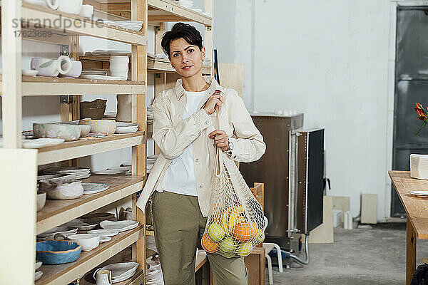 Besitzer mit einer Tüte Obst steht neben einem Holzregal in der Keramikwerkstatt