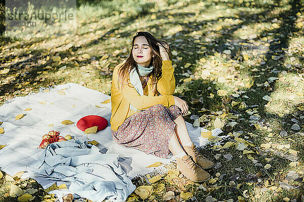 Beautiful woman with eyes closed sitting on picnic blanket at park