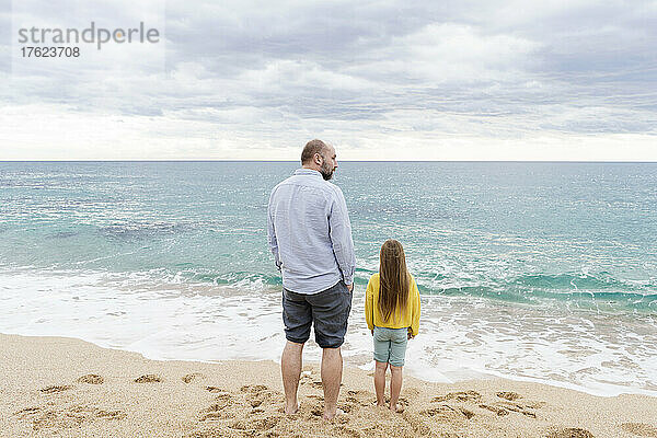 Wellen plätschern auf Vater und Tochter zu  die am Strand stehen